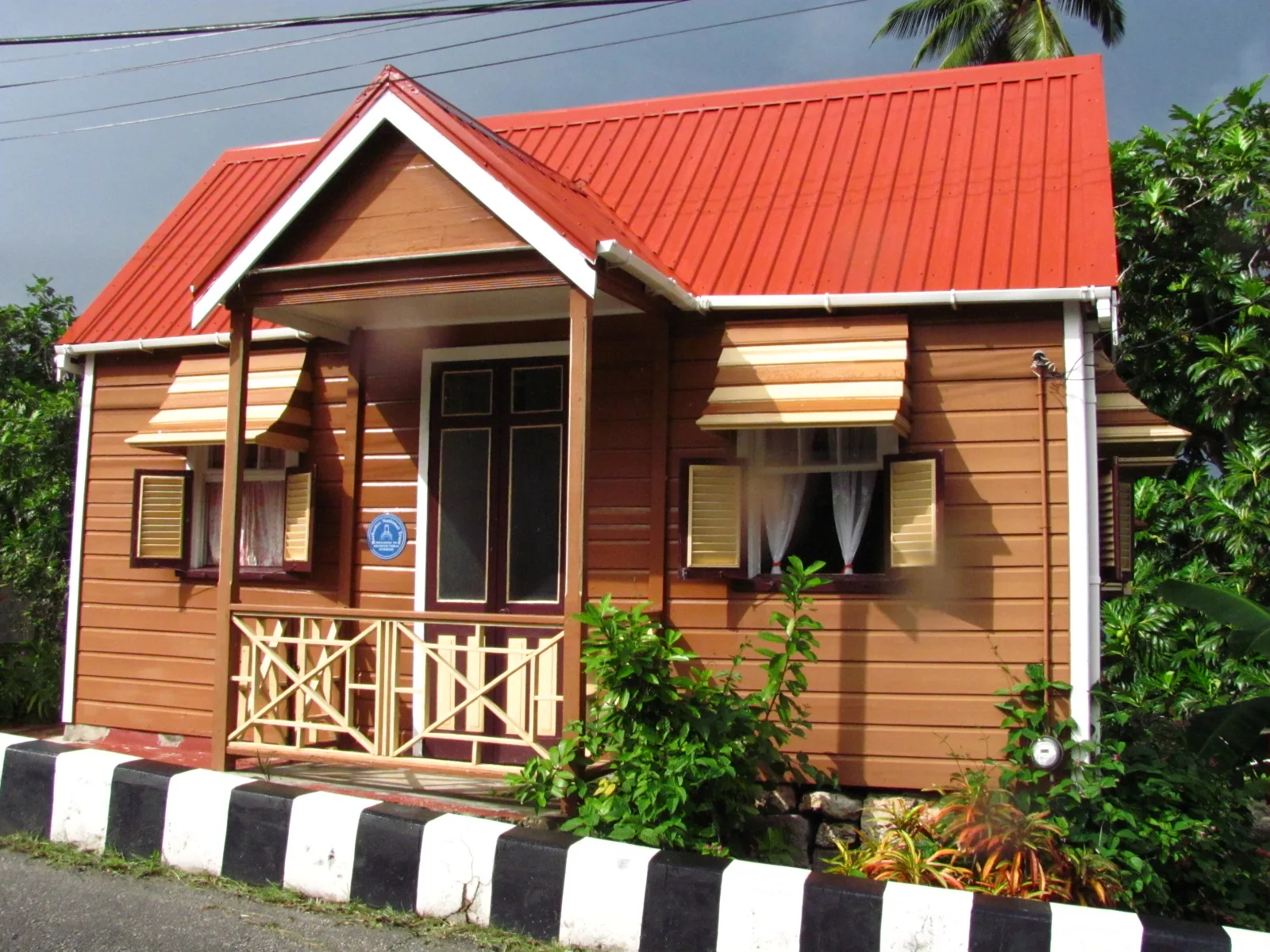 Restored Barbadian chattel house with a steep red roof, centred door and shuttered windows